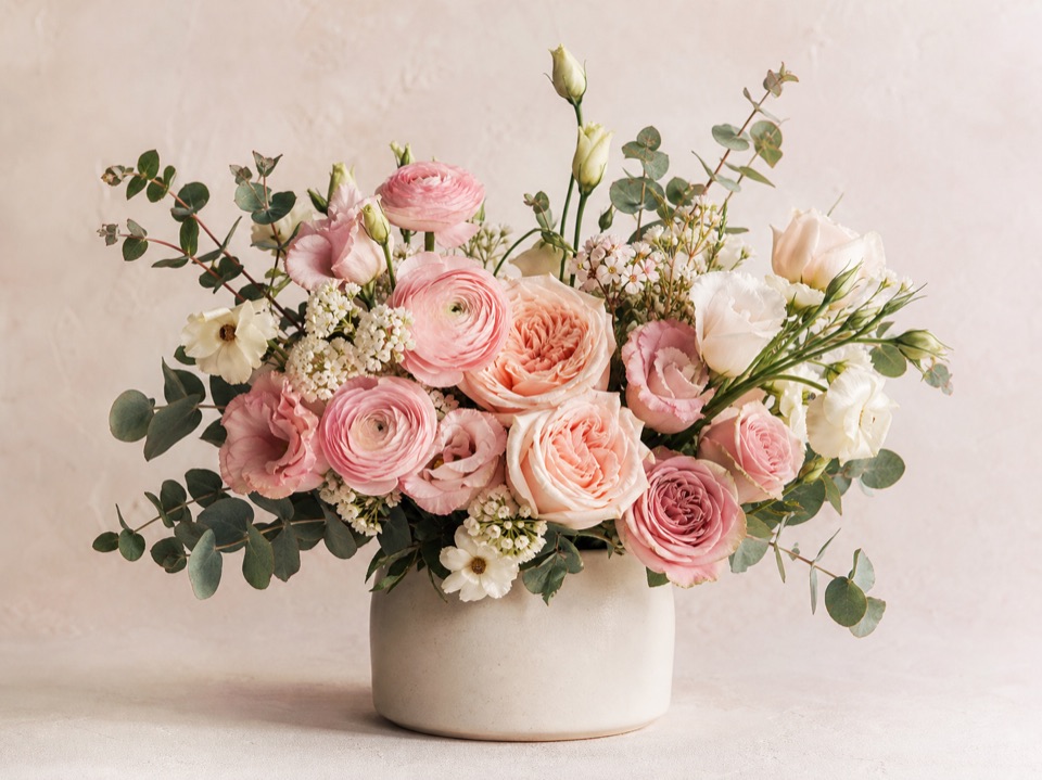Natural blush flower arrangement with roses, ranunculus, lisianthus, and eucalyptus in a cream vase